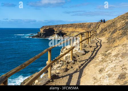Vista del sentiero costiero con una ringhiera in legno che costeggia le scogliere rocciose di Ajuy con il mare blu profondo e il cielo sereno sullo sfondo, Ajuy, Fu Foto Stock