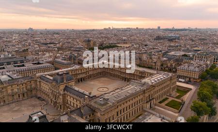 Vista a droni del cortile del Museo del Louvre al tramonto con i tetti parigini circostanti, la chiesa di Saint-Eustache e lo skyline della città in lontananza. Foto Stock