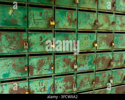 Un lucchetto in acciaio arrugginito chiuso, appeso a una cassetta postale in metallo verde logora con il numero rosso 8. Dettaglio architettonico vintage che mostra la texture della corrosione Foto Stock