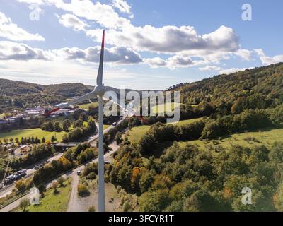 Una vista aerea mostra una turbina eolica circondata da colline e alberi durante il giorno con un'autostrada nelle vicinanze. Foto Stock