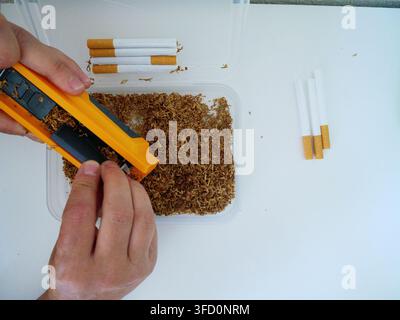 Mani di una donna che operano una macchina per arrotolare riempita con tabacco, processo di assemblaggio delle sigarette in primo piano Foto Stock