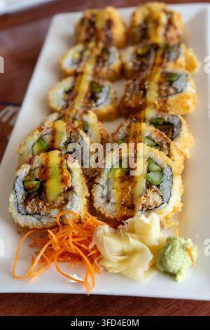 Prima verticale di involtini di sushi fritti croccanti guarniti con salsa e serviti con zenzero marinato, carota grattugiata e wasabi in un ristorante giapponese. D Foto Stock