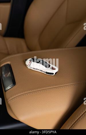 Portachiavi Porsche bianco su bracciolo in pelle beige nell'interno di un'auto di lusso Foto Stock
