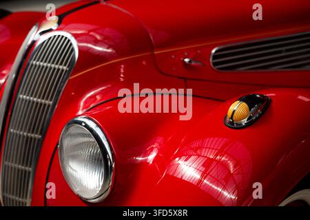 Colpo macro in primo piano del paraurti anteriore rosso curvo, della griglia cromata, del faro rotondo e della luce indicatrice ambrata di un'auto di lusso vintage impeccabile. Foto Stock