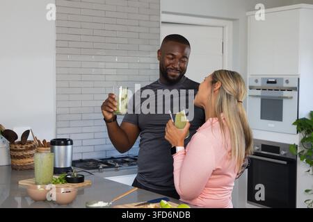 Coppia di uomo e donna afroamericani che tengono frullati verdi in cucina con abiti sportivi Foto Stock