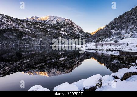 Montagne coperte di neve riflesse nell'acqua calma in una limpida mattina d'inverno a Vestland, nella Norvegia occidentale. Foto Stock