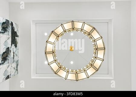 Lampadario circolare con centro dorato e pannelli luminosi. Soffitto grigio chiaro con cornice a pannello incassata. Parete in marmo aggiunge dettagli di sfondo testurizzati Foto Stock