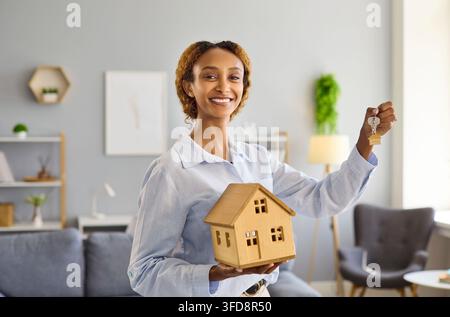 Agente immobiliare sorridente che tiene un modello di casa e le chiavi per l'acquisto di una casa Foto Stock