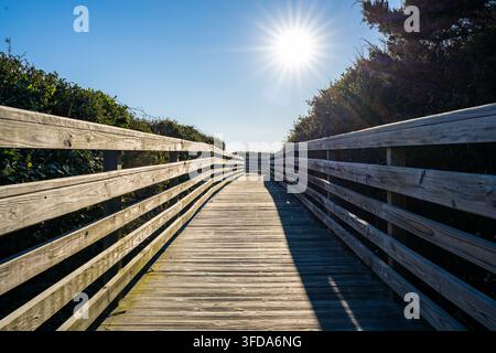 Un accesso alla spiaggia tramite una lunga passerella con il sole che splende luminoso sul sentiero verso l'oceano Foto Stock