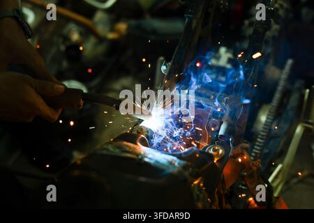 Una torcia saldatrice salda il metallo con scintille luminose in un'officina industriale buia Foto Stock