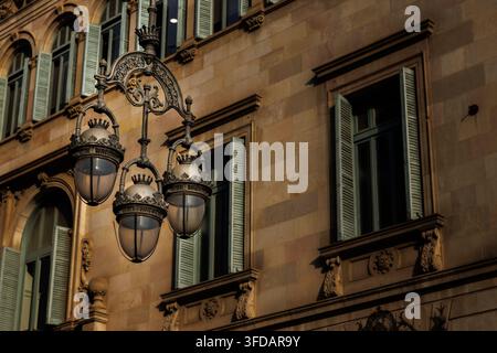 Lanterna da strada vintage ornata nel Quartiere Gotico di Barcellona, appesa a un'elegante staffa in ferro battuto davanti a una classica facciata di edificio europeo. Foto Stock
