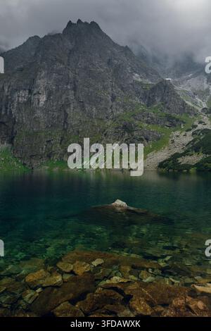 Un maestoso picco di montagna si erge sulle acque cristalline del Morskie Oko, un lago glaciale mozzafiato nella catena montuosa dei Tatri in Polonia Foto Stock