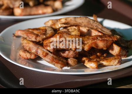 Un piatto bianco colmo di succose costine e strisce di pancetta di maiale appena grigliate, condite con pepe nero macinato, alla luce naturale del sole. Foto Stock