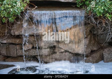 Acqua limpida che cade con grazia su un bordo di pietra impilato piatto incorniciato da una vegetazione verde rigogliosa in un bacino schiumoso sottostante Foto Stock