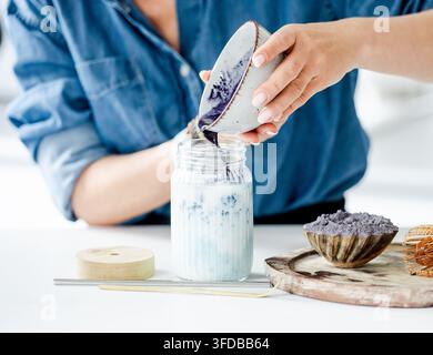 Donna che versa tè matcha blu in un barattolo con ghiaccio e latte, primo piano Foto Stock