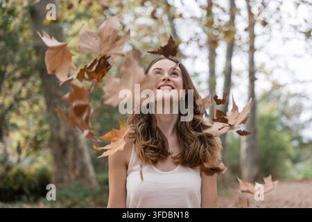 Donna che si gode le foglie autunnali che cadono nel parco Foto Stock
