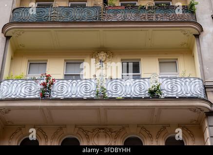 Facciata di un edificio residenziale storico con balconi decorativi, ringhiere metalliche ornate e fiori in vaso. Foto Stock