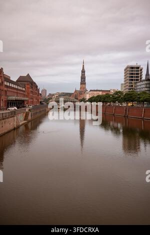 La chiesa di Santa Caterina si erge oltre il canale e l'architettura storica in mattoni vicino al quartiere di Speicherstadt di Amburgo. Foto Stock