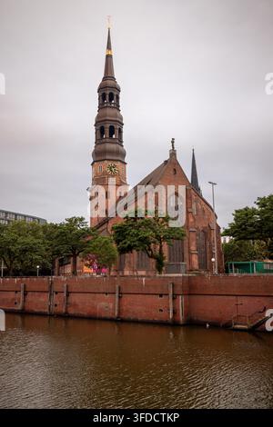 La chiesa di Santa Caterina si erge oltre il canale e l'architettura storica in mattoni vicino al quartiere di Speicherstadt di Amburgo. Foto Stock
