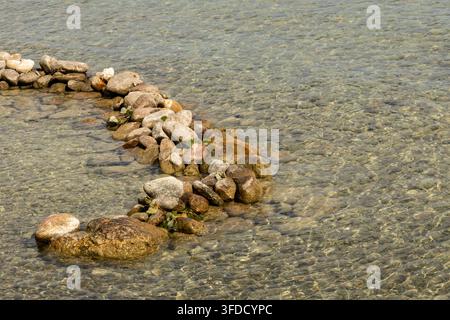 L'acqua limpida rivela pietre lisce sotto la sua superficie. Le rocce formano un sentiero tortuoso attraverso acque basse illuminate dal sole. Le pietre sono consumate, coperte di m Foto Stock
