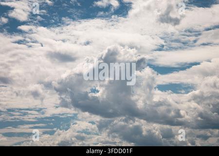 Cielo vasto pieno di soffici nuvole bianche. Macchie blu sbucano attraverso la coltre di nubi. Una luce soffusa illumina i bordi delle nuvole. Perfetto per una scena serena, pacifica, Foto Stock