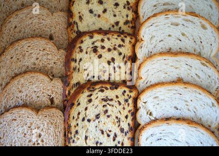 Pane tagliato assortito disposto su una superficie bianca in un ambiente da cucina con uvetta visibile, vista dall'alto, atmosfera neutra, prodotti alimentari commerciali, panetteria Foto Stock