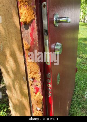 Una vista ravvicinata di una porta di sicurezza o di una cassaforte danneggiata, posizionata orizzontalmente all'aperto su travi di legno. La porta presenta un metallo bruno-rosso Foto Stock
