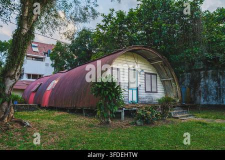 Balikpapan, Indonesia - 7 agosto 2026. Vista esterna di un edificio in stile capanna Quonset vintage con tetto in lamiera ondulata e pareti in legno, circondato Foto Stock