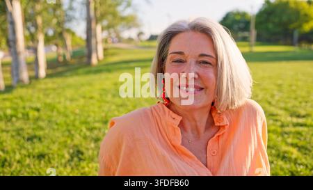 Donna anziana sorridente nel parco che gode della luce del tramonto Foto Stock