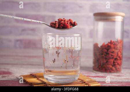 Bacche di Goji su un cucchiaio sopra acqua nel bicchiere Foto Stock