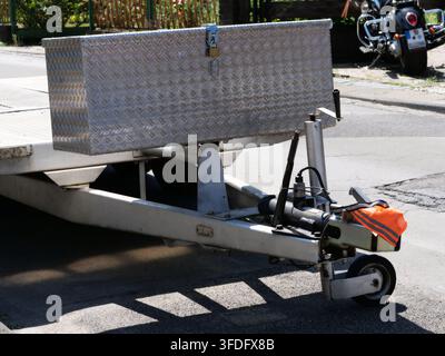 Scatto ravvicinato dettagliato che si concentra sul meccanismo di accoppiamento anteriore di un rimorchio trasportatore di auto. Evidenzia la cassetta degli attrezzi in piastra a scacchi di alluminio bloccata, h Foto Stock