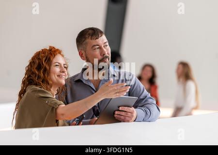 Donna sorridente indica qualcosa a un uomo con un tablet Foto Stock