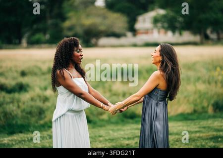 Due amiche donne diverse che si tengono per mano in un campo Foto Stock
