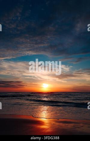 Sole infuocato che tramonta sulle onde dell'oceano sulla spiaggia Foto Stock