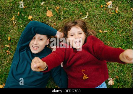 Fratelli e sorelle felici sdraiati sull'erba autunnale circondati da foglie cadute Foto Stock