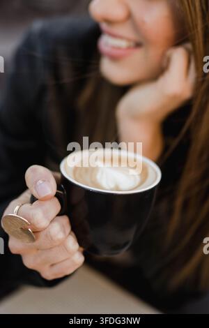 Donna che tiene una tazza di caffè con latte art a forma di cuore Foto Stock