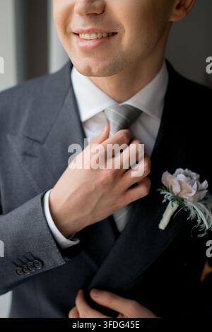 Sposo sorridente che sistema la sua cravatta prima del matrimonio Foto Stock