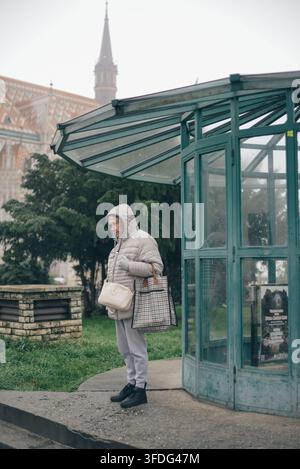 Anziana in attesa a una fermata dell'autobus in una giornata nuvolosa Foto Stock