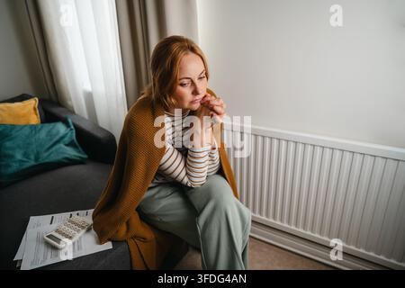 Donna stressata seduta da sola a casa preoccupata per le bollette Foto Stock