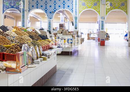 Frutta secca e noci esposte in mucchi in un bazar interno a Bukhara, Uzbekistan. Archi ornamentali con mosaici di piastrelle colorate incorniciano il spazioso m Foto Stock