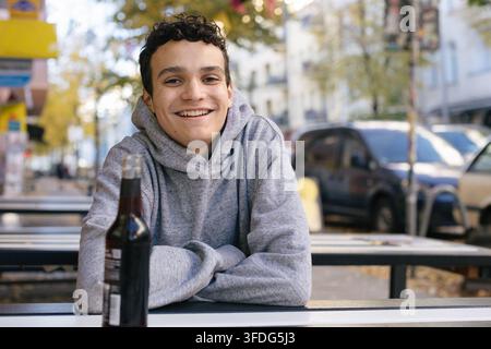 Giovane uomo felice in una felpa con cappuccio che sorride in un caffè all'aperto Foto Stock