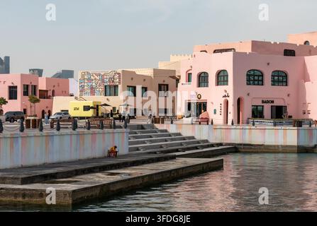 Doha, Qatar - 1 febbraio 2026: Un primo piano dettagliato di vivaci edifici sul lungomare in tonalità pastello, con visitatori che esplorano. Foto Stock