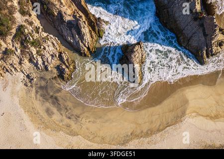Vista aerea della costa rocciosa e della spiaggia sabbiosa con onde che si infrangono e acqua limpida a Maruata, Michoacán, Messico. Foto Stock