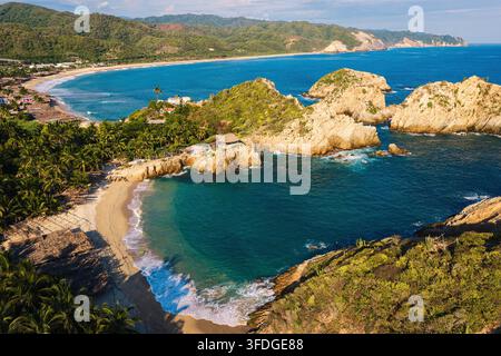 Vista aerea della spiaggia di Maruata con le sue acque turchesi, scogliere rocciose e palme lussureggianti lungo la costa a Maruata, Michoacán, Messico. Foto Stock