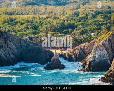 Vista aerea della formazione rocciosa Dedo de Dios che si erge dal mare turchese, con una spiaggia sabbiosa, palme dense e colline verdi lussureggianti sullo sfondo Foto Stock