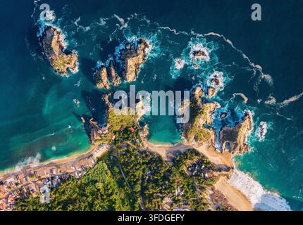 Vista aerea della costa frastagliata e delle acque turchesi di Maruata con isolotti rocciosi, spiagge di sabbia e vegetazione lussureggiante a Maruata, Michoacan, Messico Foto Stock