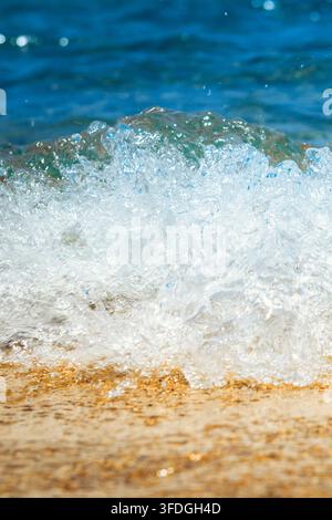 Vista ravvicinata di un'onda del mare che rotola dolcemente su una spiaggia di sabbia, con l'acqua schiumosa dell'oceano che si sparge lungo la linea costiera. Scena costiera naturale con Foto Stock