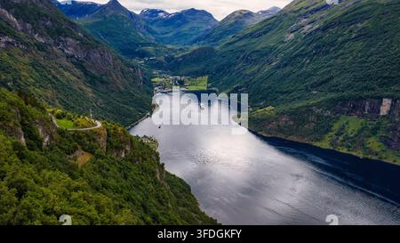 Prospettiva aerea di una profonda valle fjord con acqua blu-grigia, fitta foresta verde su pareti rocciose ripide, piccoli insediamenti lungo la riva, crociera. Foto Stock