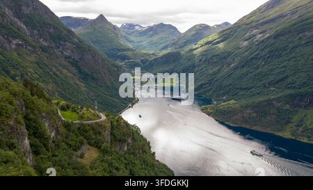 Prospettiva aerea di un profondo fiordo norvegese circondato da ripide montagne verdi, con più navi da crociera ancorate in acque calme e piccole. Foto Stock