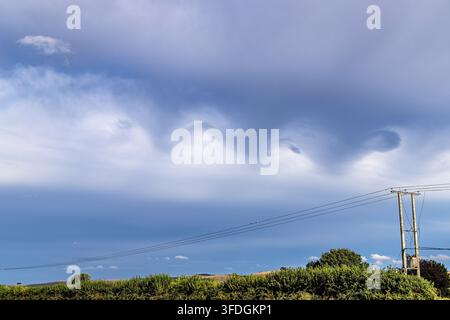 Nuvole di tempesta drammatiche e ondulate che formano schemi a onde sopra un paesaggio rurale. Foto Stock